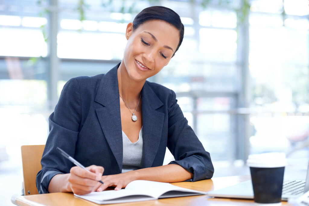 Smile, business woman and writing in notebook, research and information in office. Journal, notes and professional secretary at desk with pen for reminder, schedule and planning ideas for project.